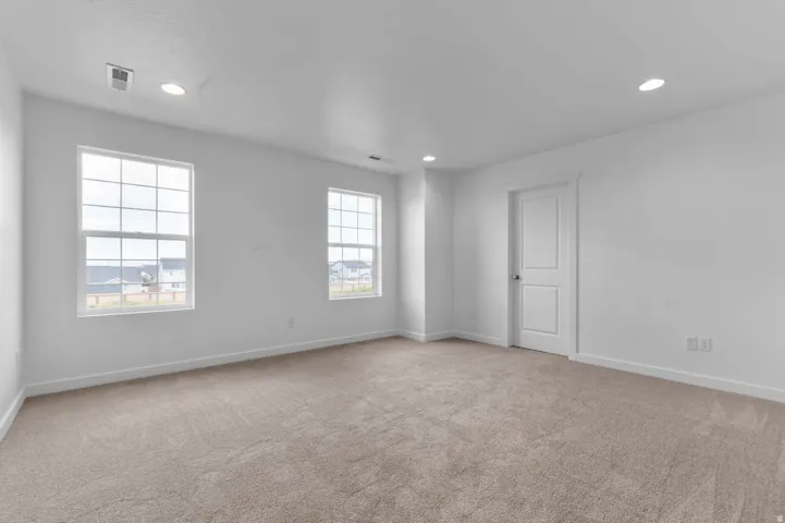 Spacious room featuring neutral carpet flooring, two large multi-pane windows, recessed ceiling lighting, and a two-panel interior door with white trim