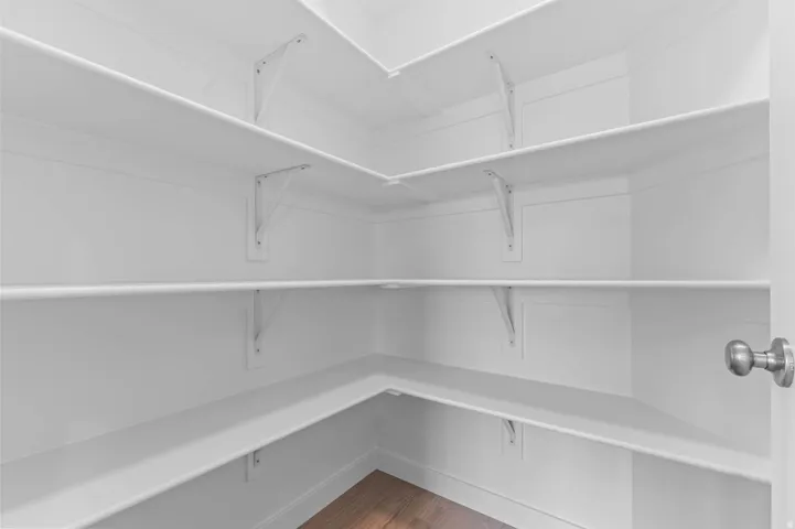 Walk-in pantry featuring white shelving, white walls, and wood-finish flooring