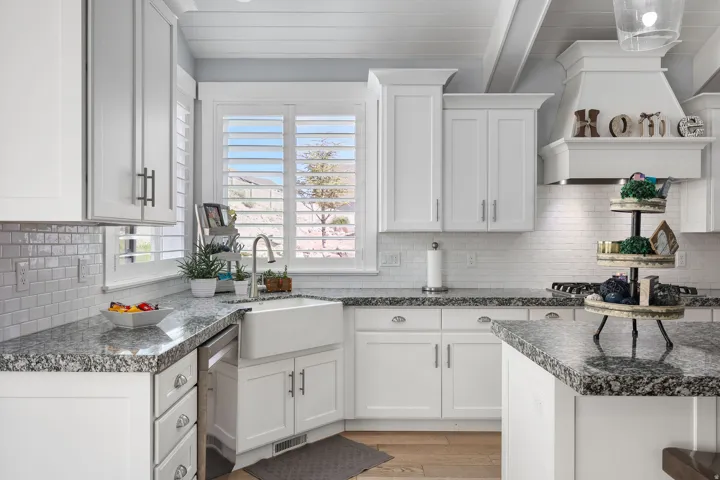 Kitchen featuring white shaker cabinetry, speckled granite countertops, a farmhouse-style sink, and a tiled backsplash
