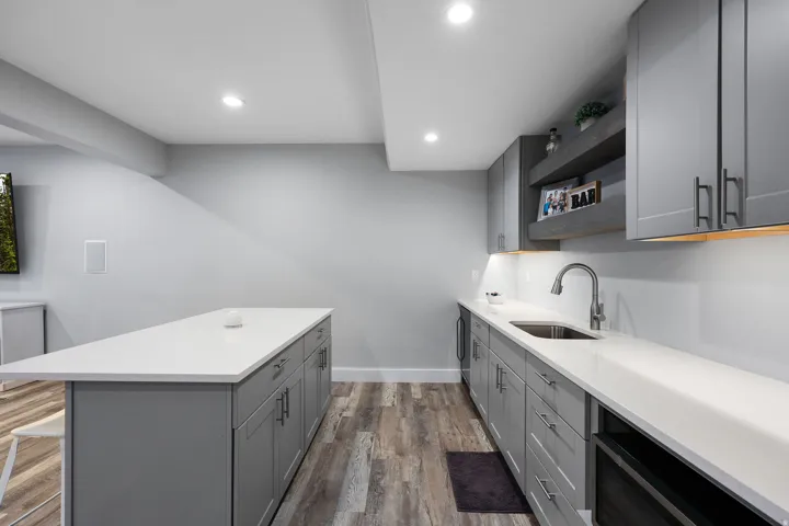 Modern entertainment space featuring an expansive island with white countertops, grey shaker-style cabinetry, and wood-finish flooring