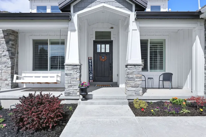 Inviting front entry featuring a covered porch, stone veneer accents, and a dark paneled door with glass inserts