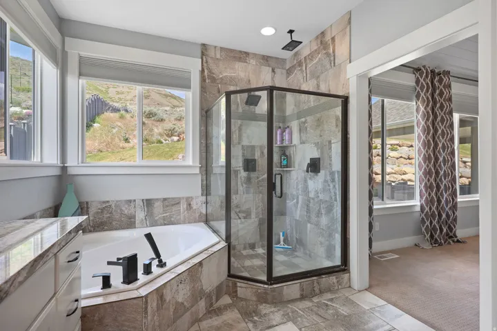 Spacious bathroom featuring a corner soaking tub with matte black fixtures, a glass-enclosed shower with tiled walls, and a vanity with a stone-finish countertop