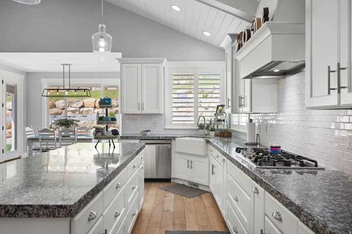 Modern kitchen featuring white cabinetry, granite countertops, a farmhouse sink, stainless steel appliances, and wood-finish flooring