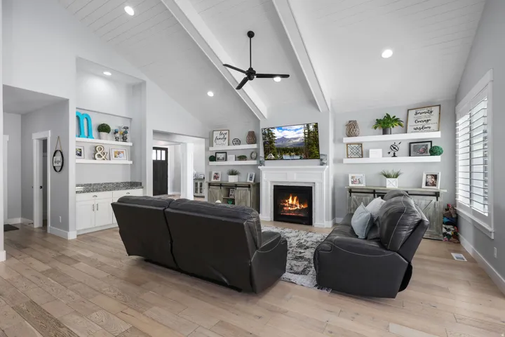 Spacious living area featuring high vaulted ceilings with exposed beams, wood-finish flooring, a fireplace with a white mantel, and built-in shelving with cabinetry