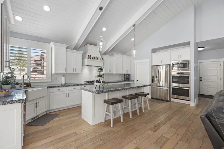 Spacious kitchen featuring white cabinetry, granite countertops, a farmhouse sink, stainless steel appliances, and wood-finish flooring