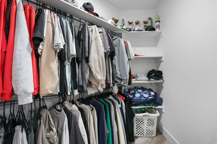 Walk-in closet with multiple hanging rods, extensive white shelving, and wood-finish flooring