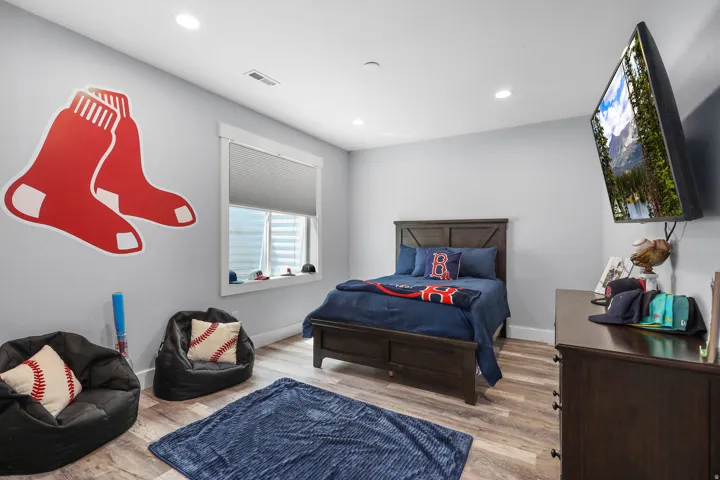 Recessed lighting illuminates a room featuring wood-finish flooring, light gray wall paint, and white trim