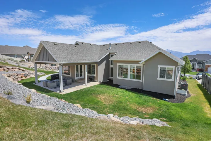 Expansive backyard featuring a covered patio, manicured lawn, and multi-level landscaping with rock retaining walls