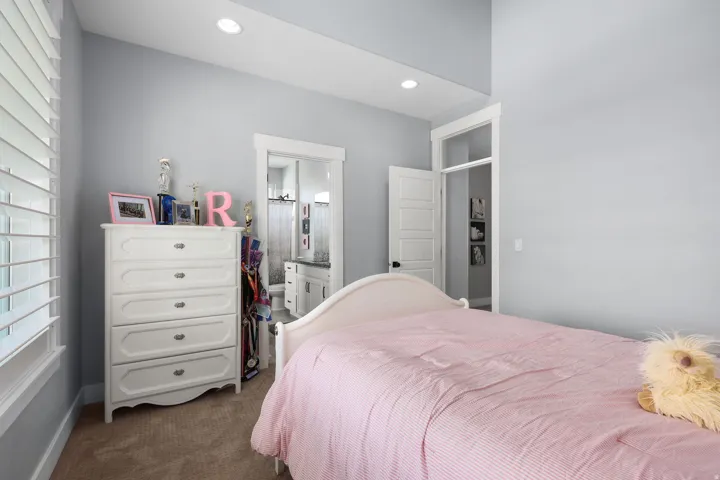 Carpeted room featuring a window with white plantation shutters, recessed lighting, and a doorway leading to a bathroom with a vanity and mirror