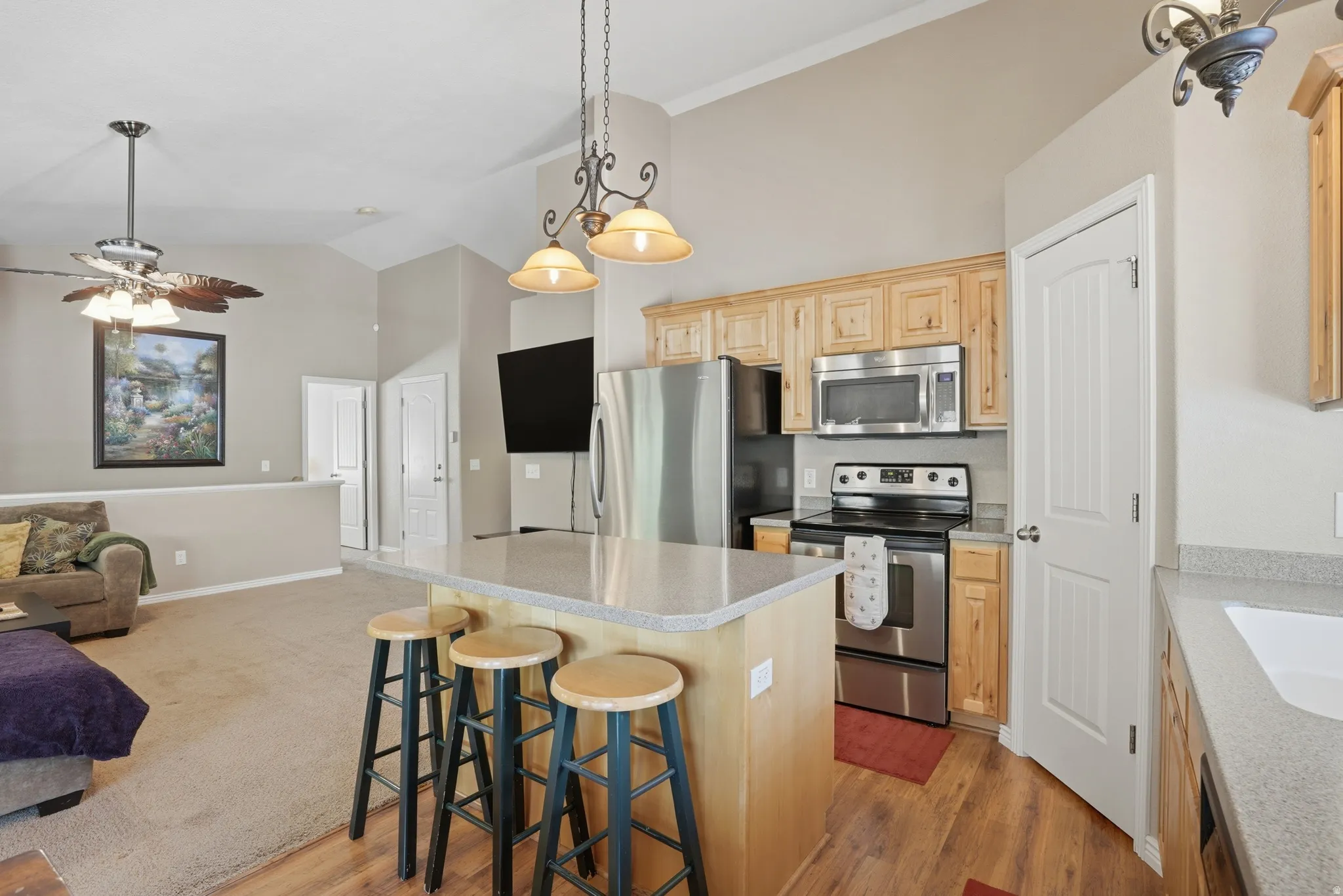 Kitchen featuring a central island with countertop seating, stainless steel appliances, light wood cabinetry, and wood-finish flooring
