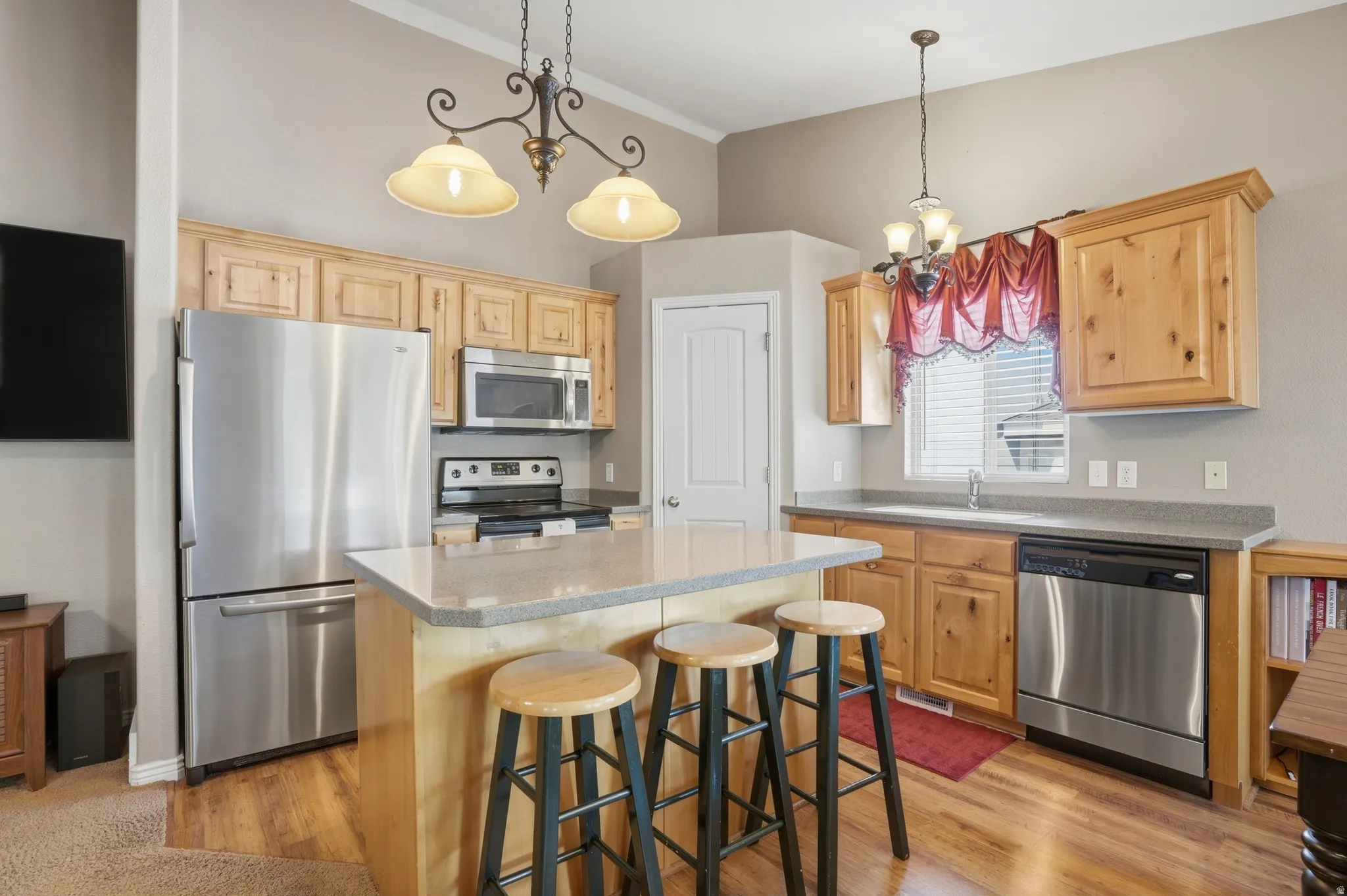 Kitchen featuring wood-finish flooring, stainless steel appliances, light wood cabinetry, a central island with countertop seating, and recessed lighting