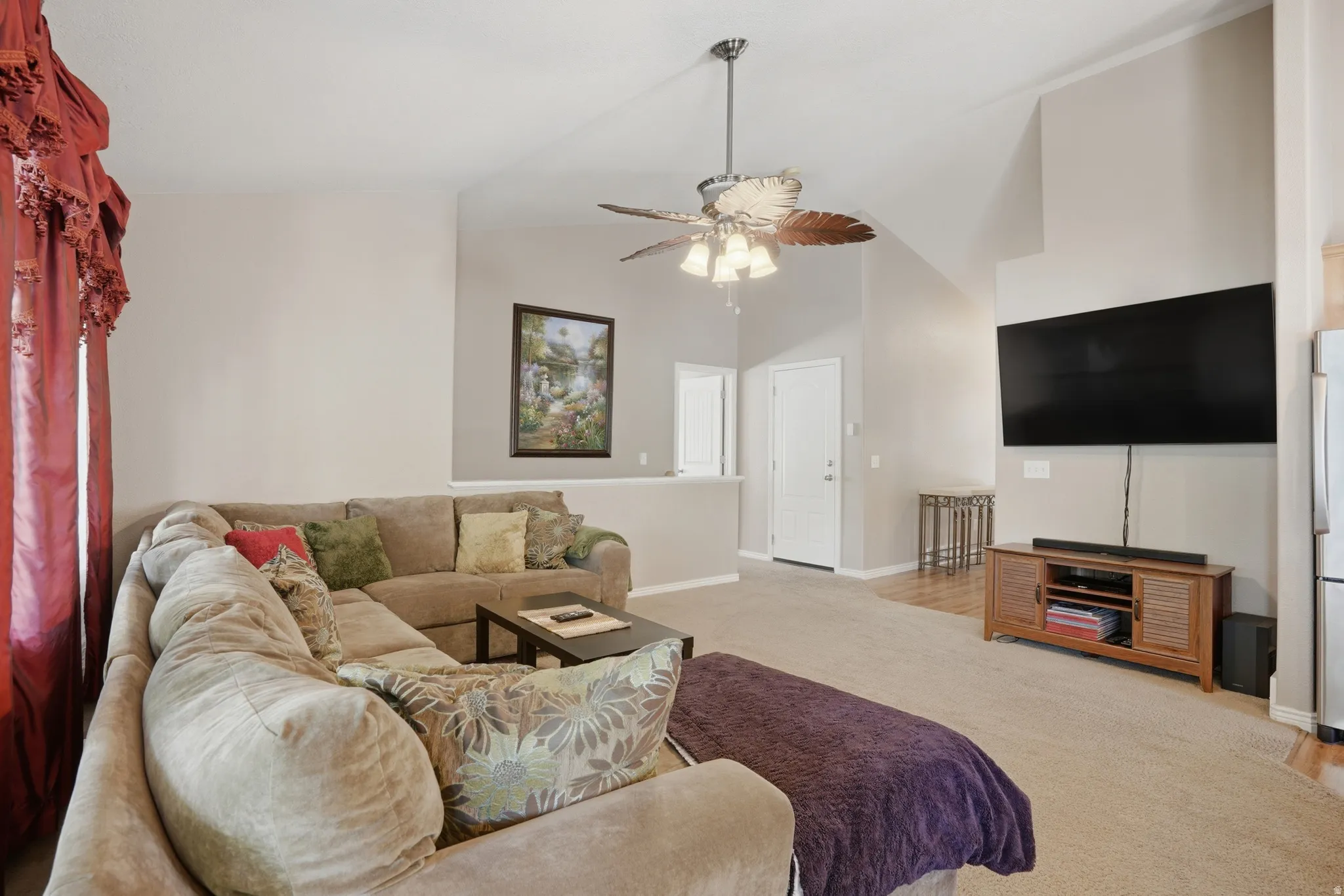 Living area featuring vaulted ceilings, a ceiling fan with light fixture, carpeted flooring, and a half-wall partition