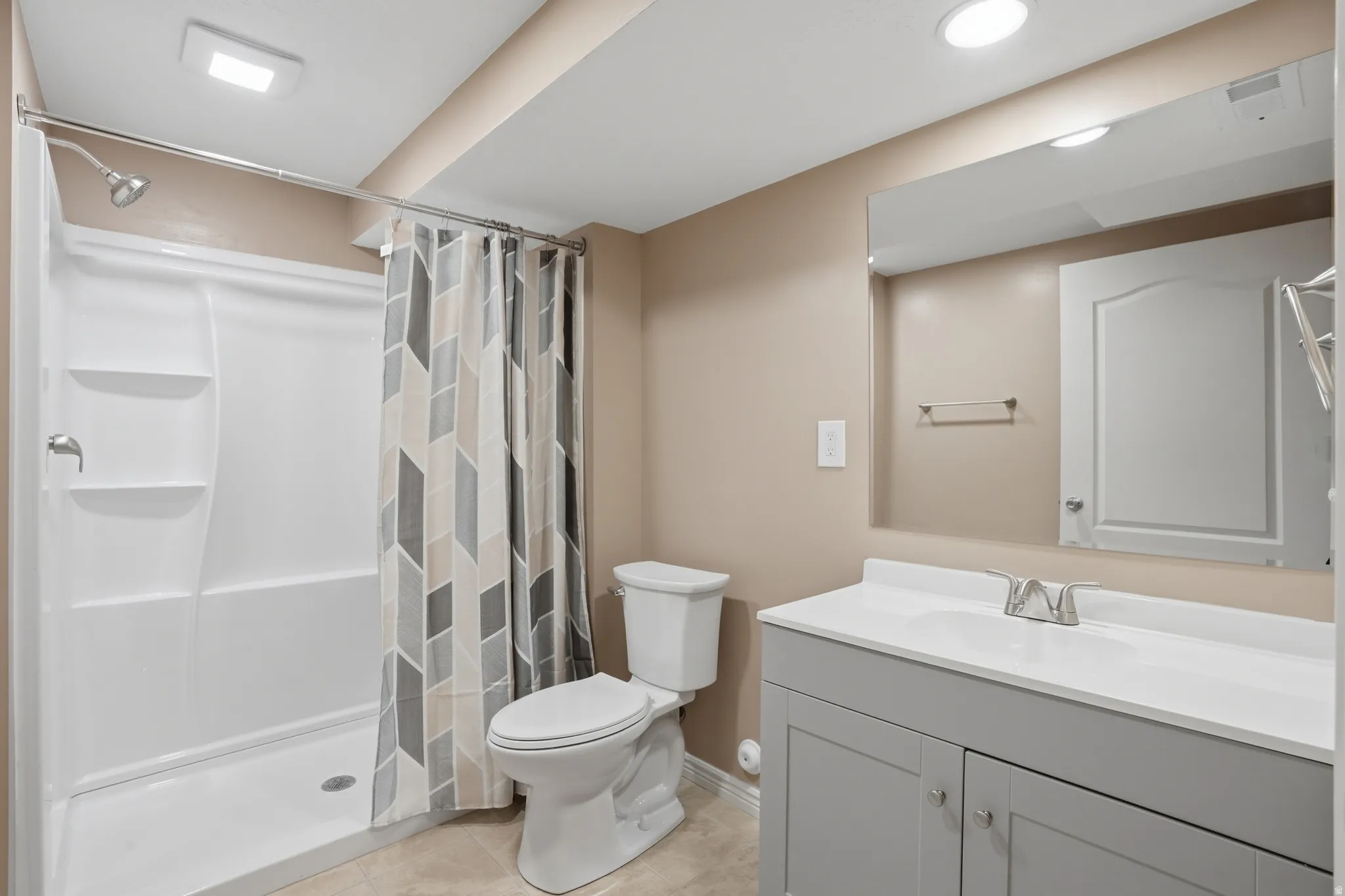 Bathroom featuring a white shower with built-in shelving, a light gray vanity with a white countertop and integrated sink, a large mirror, and recessed ceiling lighting