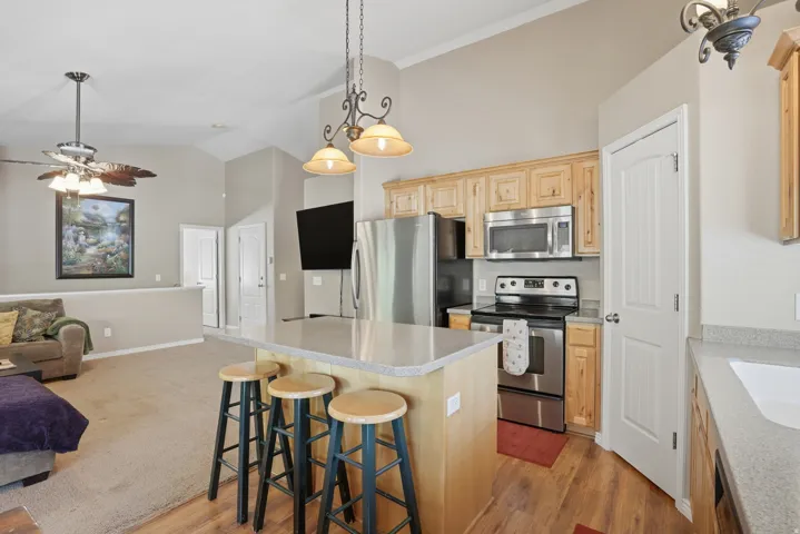 Kitchen featuring a central island with countertop seating, stainless steel appliances, light wood cabinetry, and wood-finish flooring