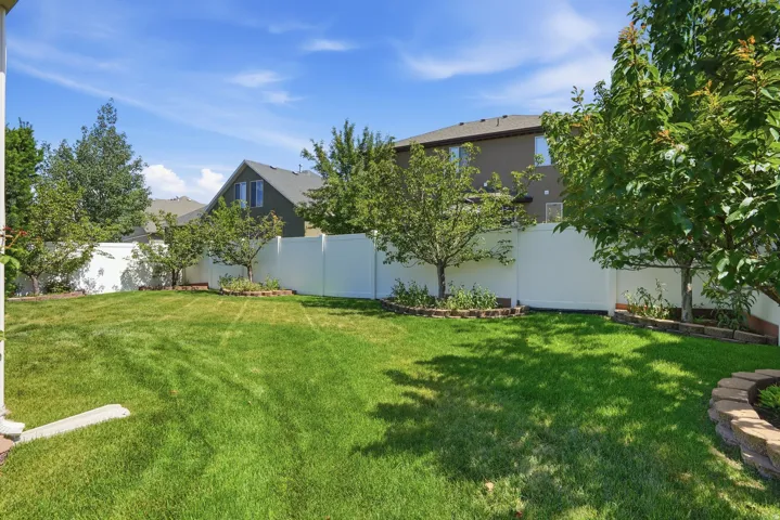 Expansive green lawn with mature trees and a white privacy fence