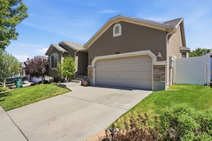 Stucco exterior featuring a two-car garage with an overhead door, a concrete driveway, and a front lawn with mature landscaping