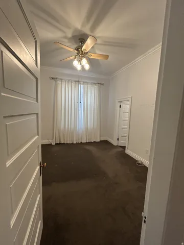 Bedroom featuring a ceiling fan with light fixture, white crown molding, and a paneled door