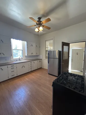 Kitchen featuring wood-finish flooring, white cabinetry with dark hardware, stainless steel refrigerator, and a ceiling fan with integrated lighting