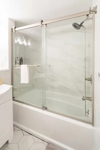 Bathtub with sliding glass shower door, brushed nickel hardware, and a rainfall showerhead
