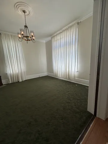 Spacious room with dark green carpeting, featuring a decorative ceiling medallion and a chandelier light fixture