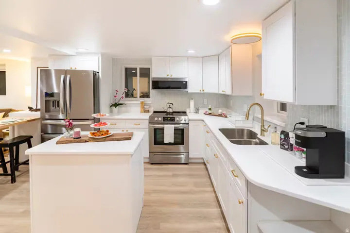 Modern kitchen featuring a central island, white cabinetry, stainless steel appliances, light-toned wood-finish flooring, and a subway tile backsplash