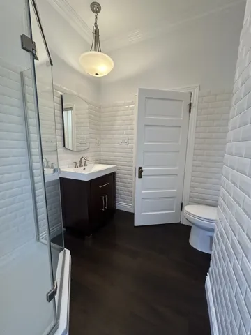 Bathroom featuring a glass-enclosed shower, dark wood-finish vanity with a white countertop, and subway tile walls