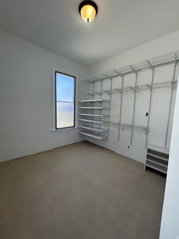 Room with neutral carpet flooring, white walls, a single window, and a built-in wire shelving system