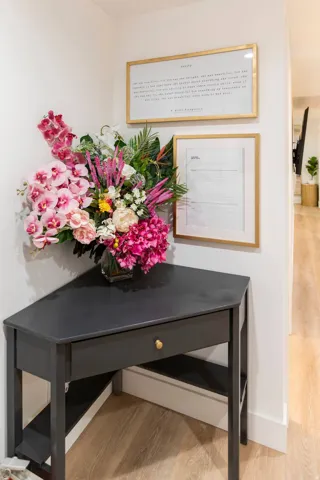 Corner console table with a single drawer and lower shelving, set against a white wall with light wood-finish flooring