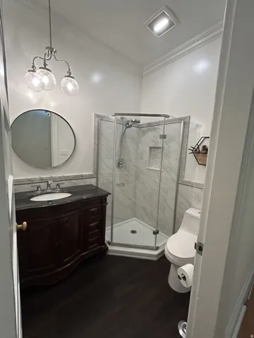 Full bathroom featuring a dark wood-finish vanity with a dark countertop, an enclosed corner shower with glass panels and marble-look tile, and dark wood-finish flooring