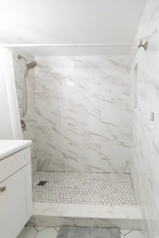 Shower stall featuring large format marbled tile walls and a hexagonal mosaic tile floor