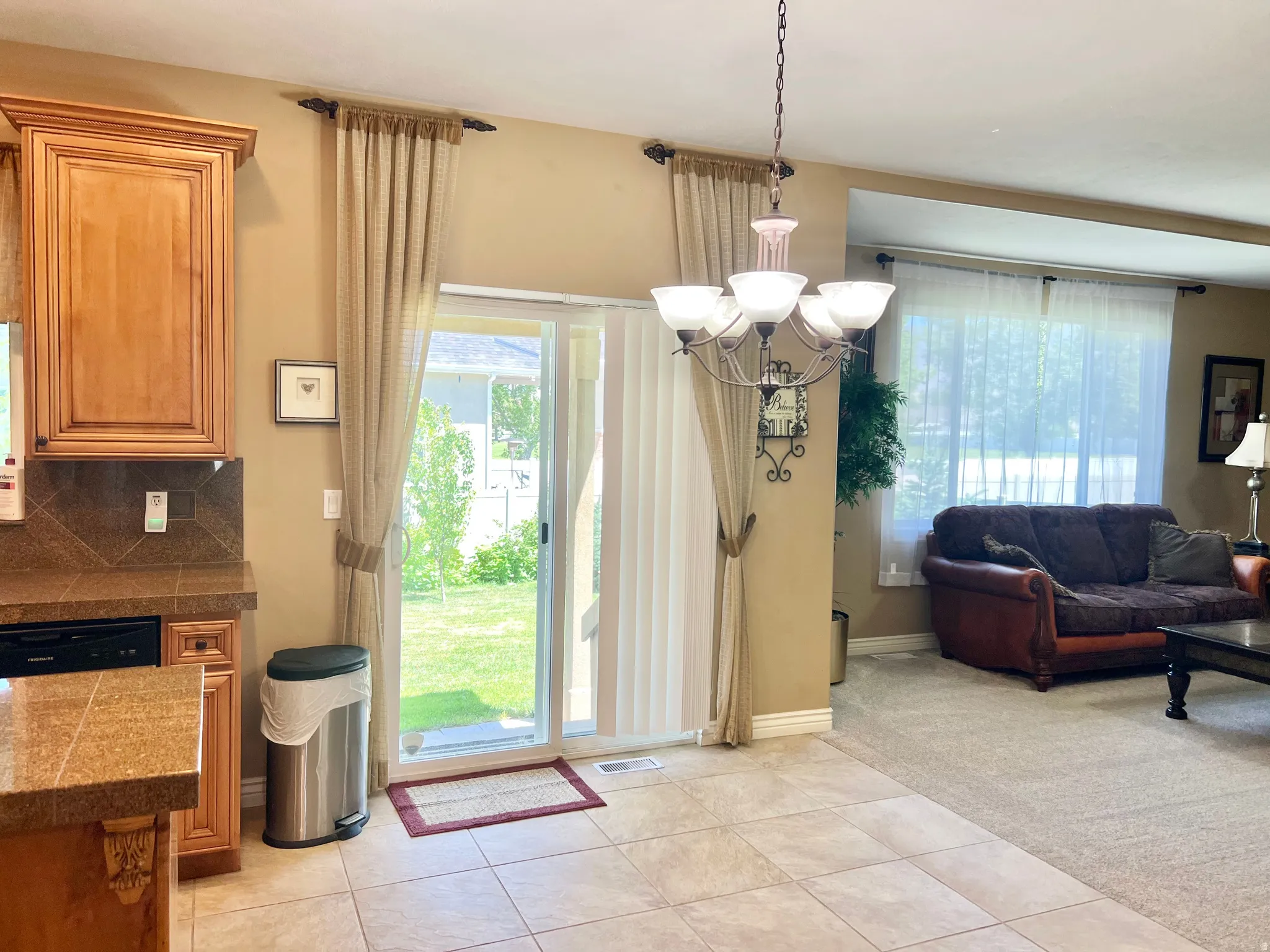 Open-concept living area featuring a tile floor, wood cabinetry, built-in dishwasher, and a chandelier