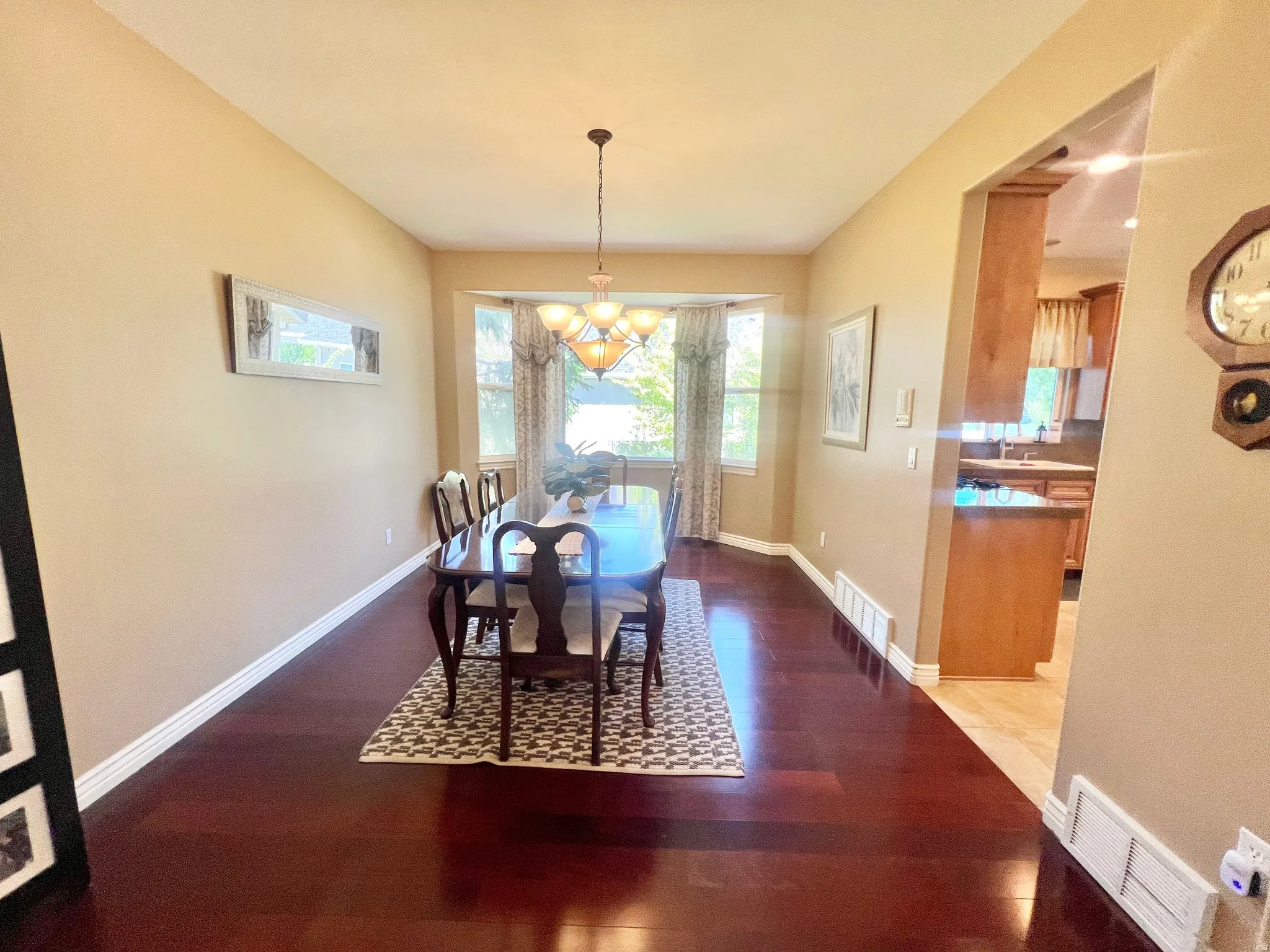 Dining area featuring rich wood-finish flooring, a bay window with natural light, and a prominent overhead chandelier
