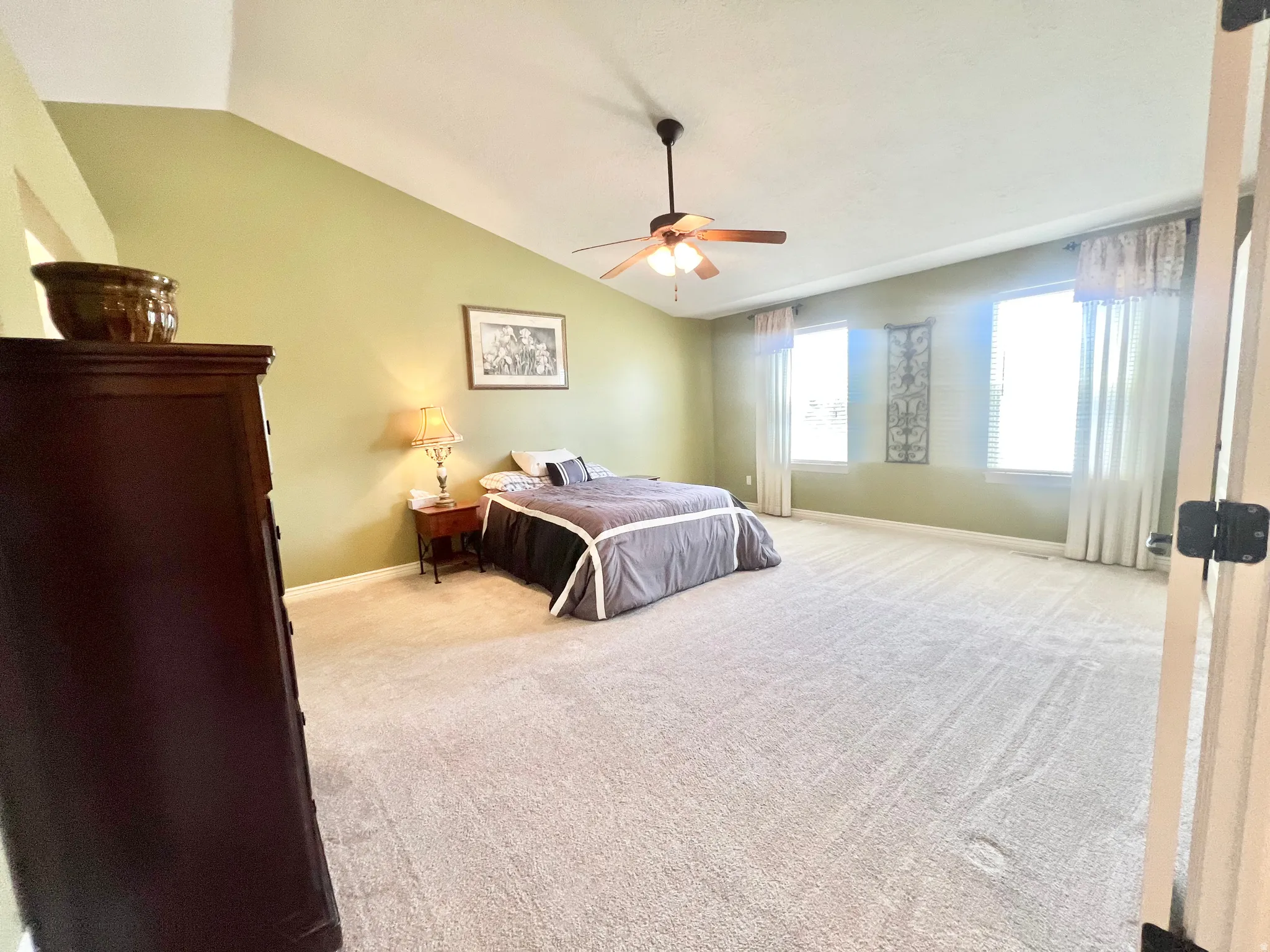 Spacious bedroom featuring vaulted ceilings, light green wall tones, neutral carpet flooring, and a ceiling fan with integrated lighting