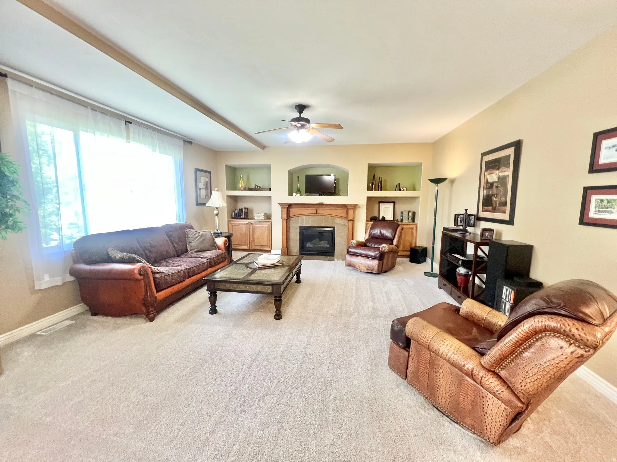 Living area featuring a fireplace with a wood mantle and stone surround, built-in shelving, recessed wall niches, a ceiling fan, and carpet flooring