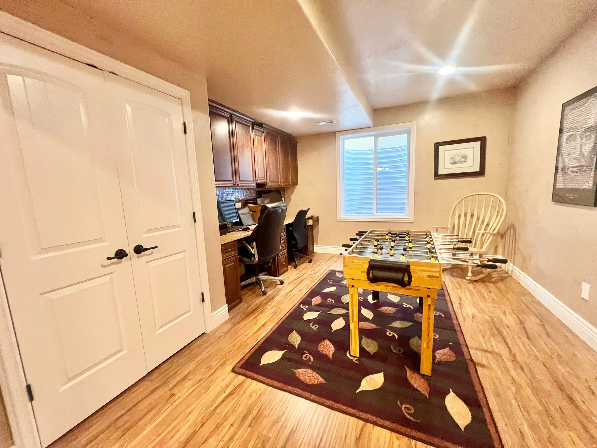 Versatile room featuring wood-finish flooring and a built-in desk with overhead cabinetry