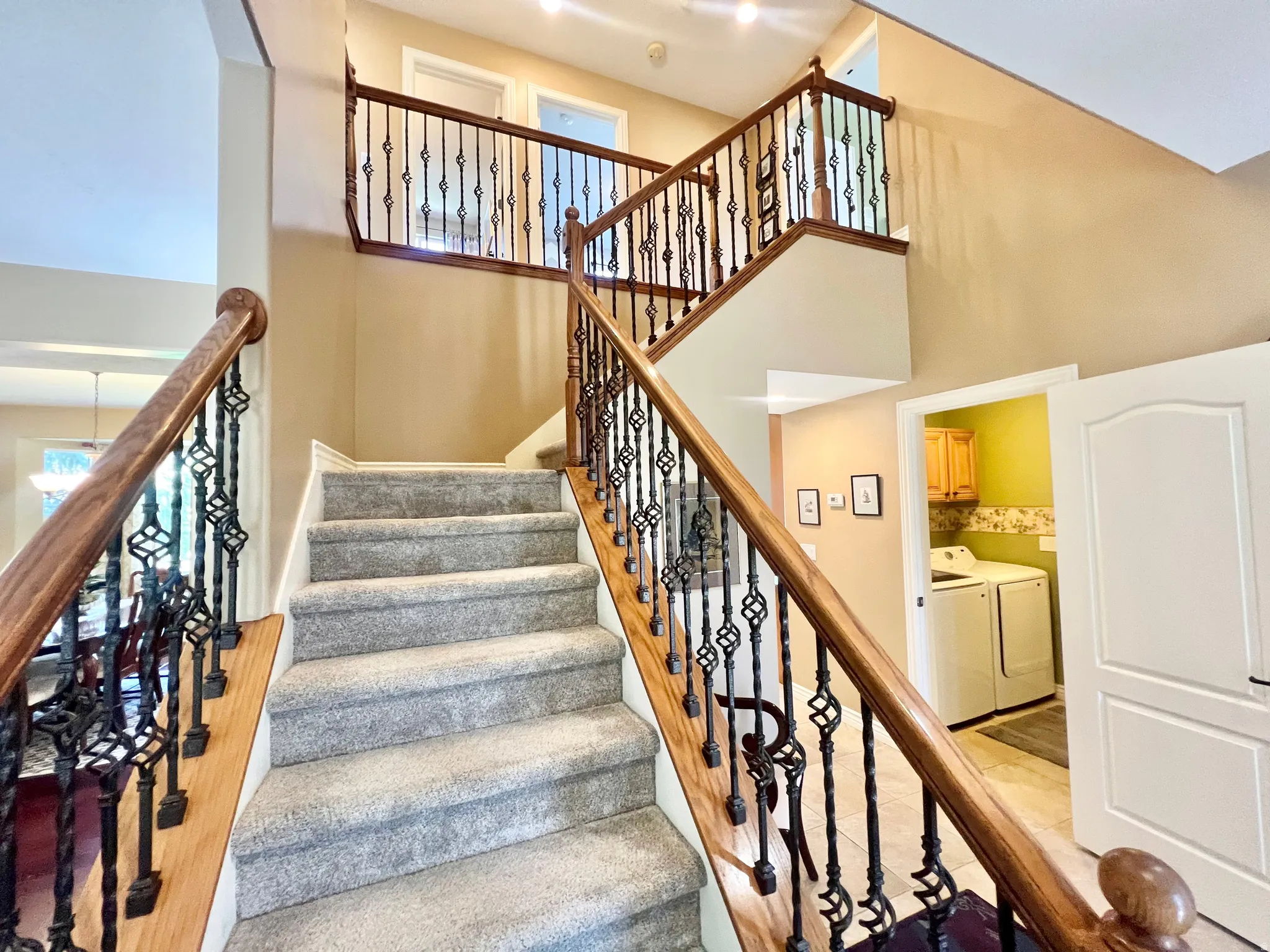 Grand staircase featuring carpeted treads, wood-finish handrails, and decorative wrought iron balusters