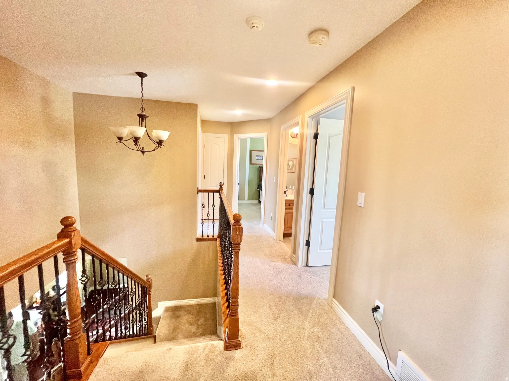 Carpeted landing featuring a chandelier light fixture, wood-finish handrail, and wrought-iron balusters