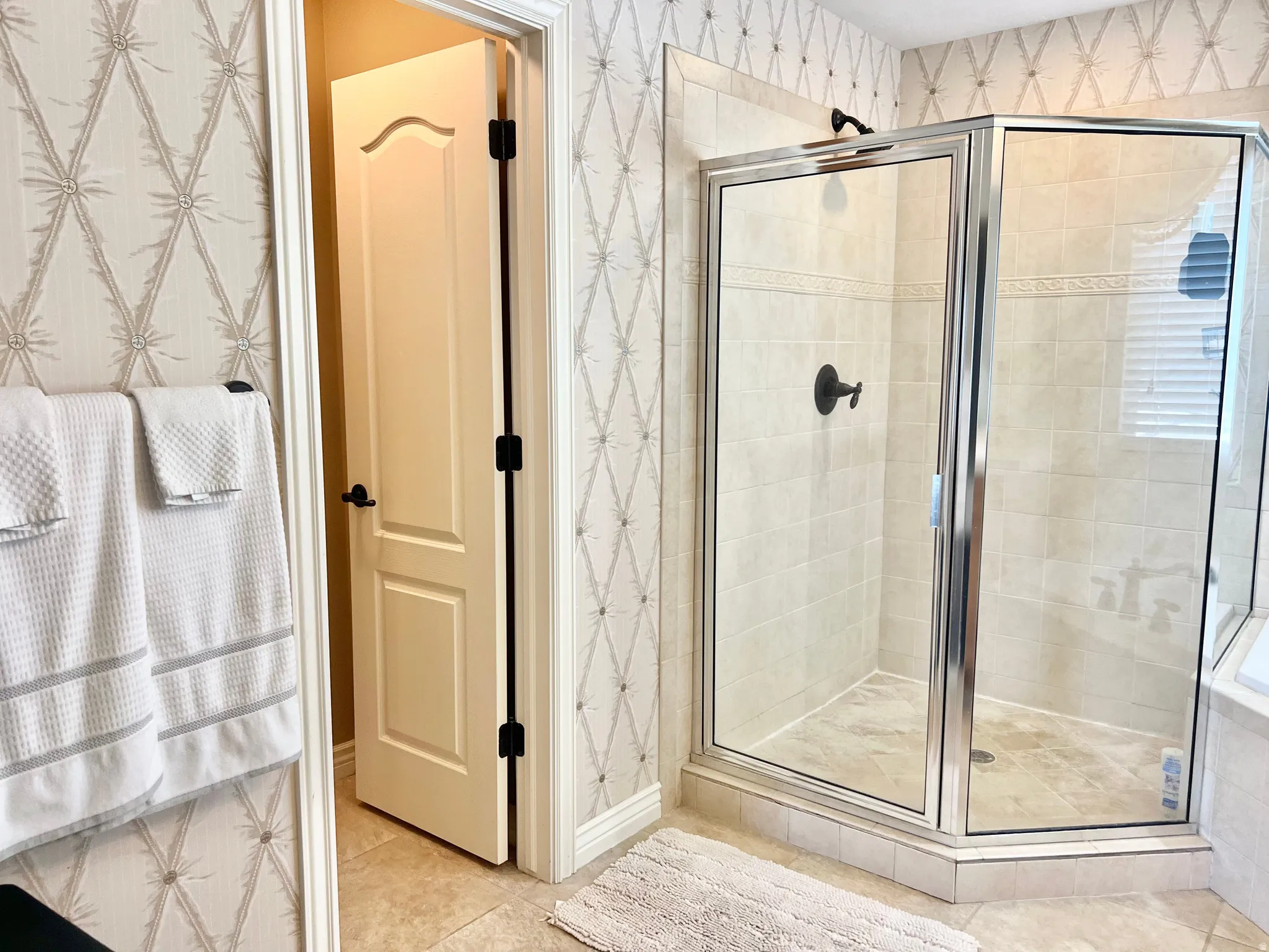Glass-enclosed shower featuring light-toned tile walls and flooring, complemented by matte black fixtures