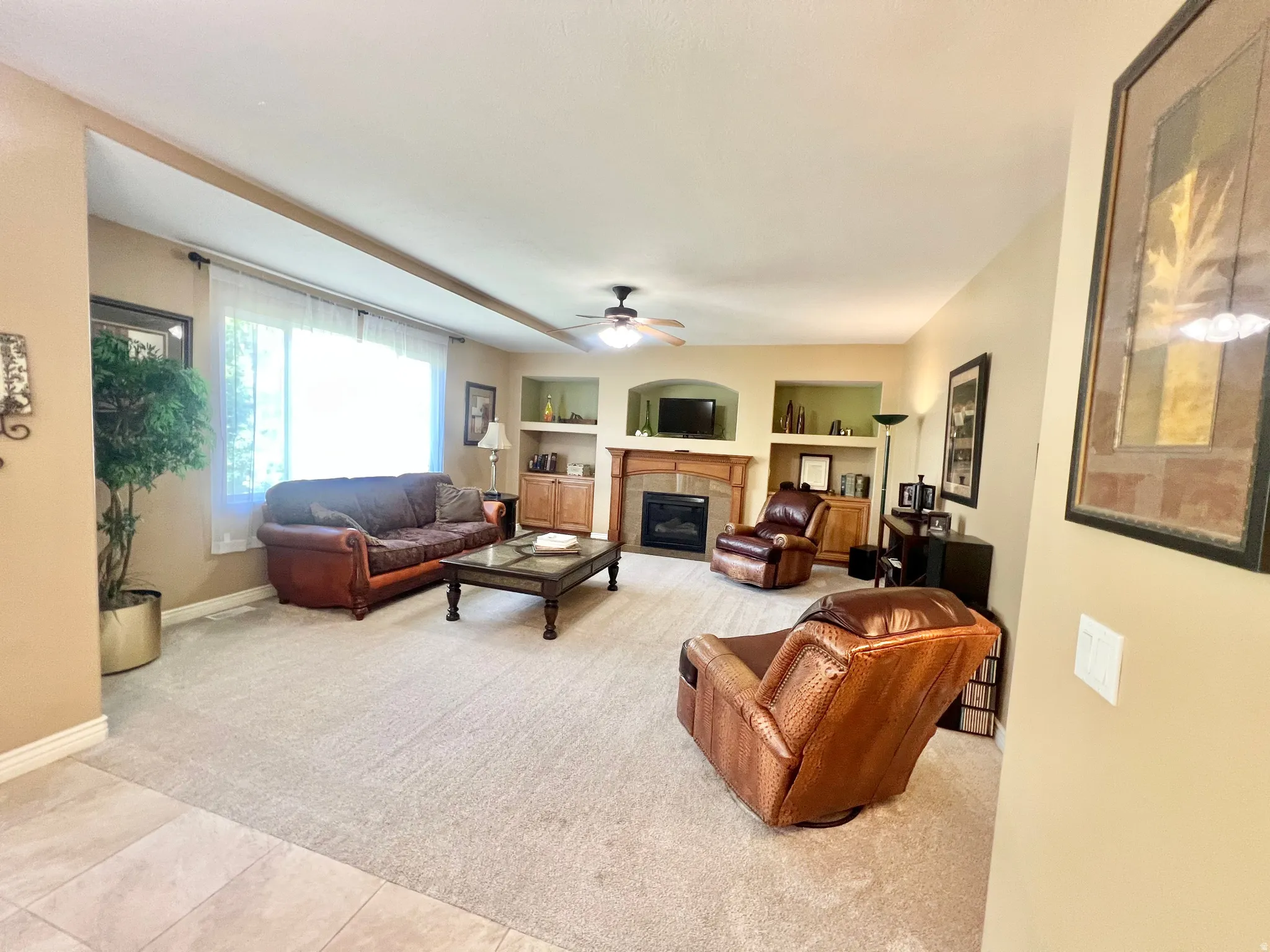 Carpeted living area featuring a built-in fireplace with a wood mantel, recessed shelving, and a large window with sheer treatments