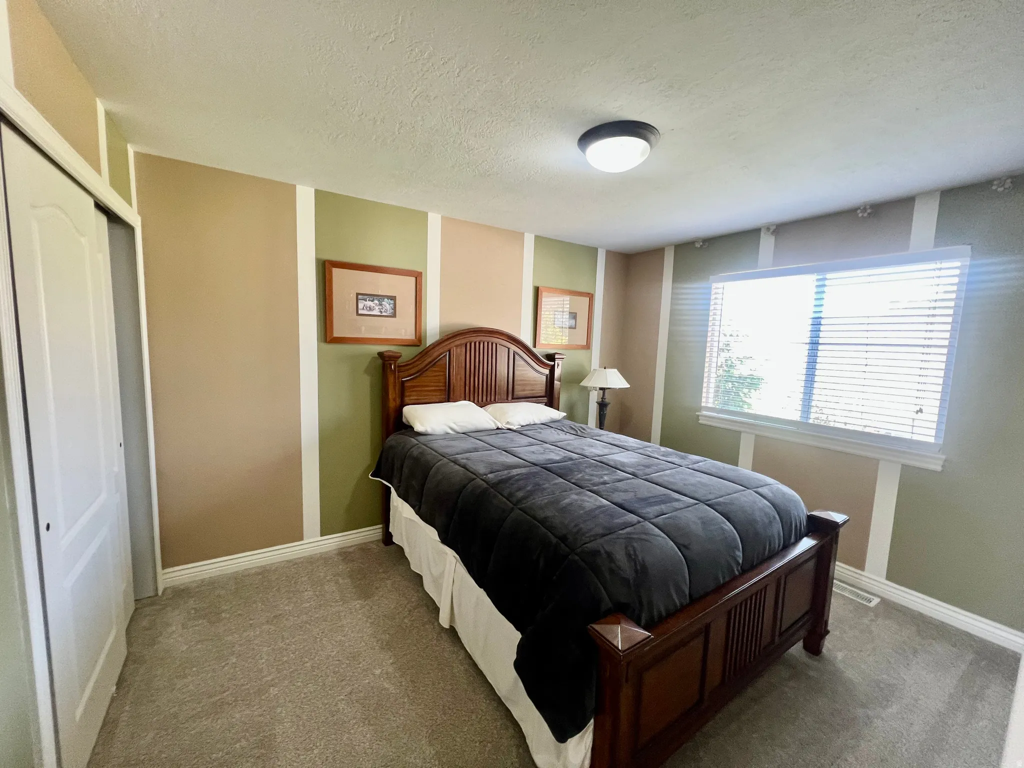 Carpeted bedroom featuring a large window with blinds, bi-fold closet doors, and decorative wall paneling