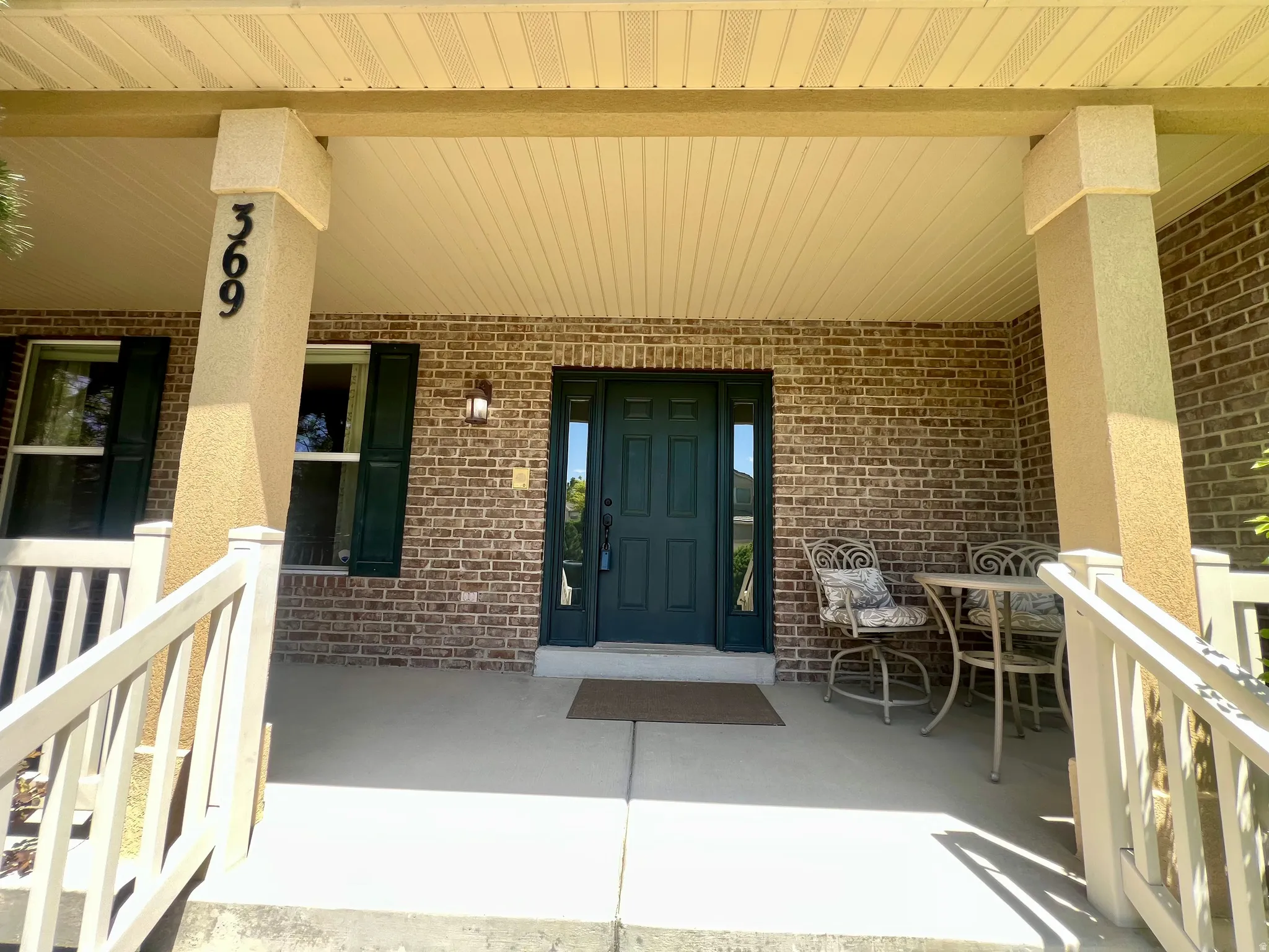 Inviting front porch featuring brick siding and a dark green entry door with sidelights