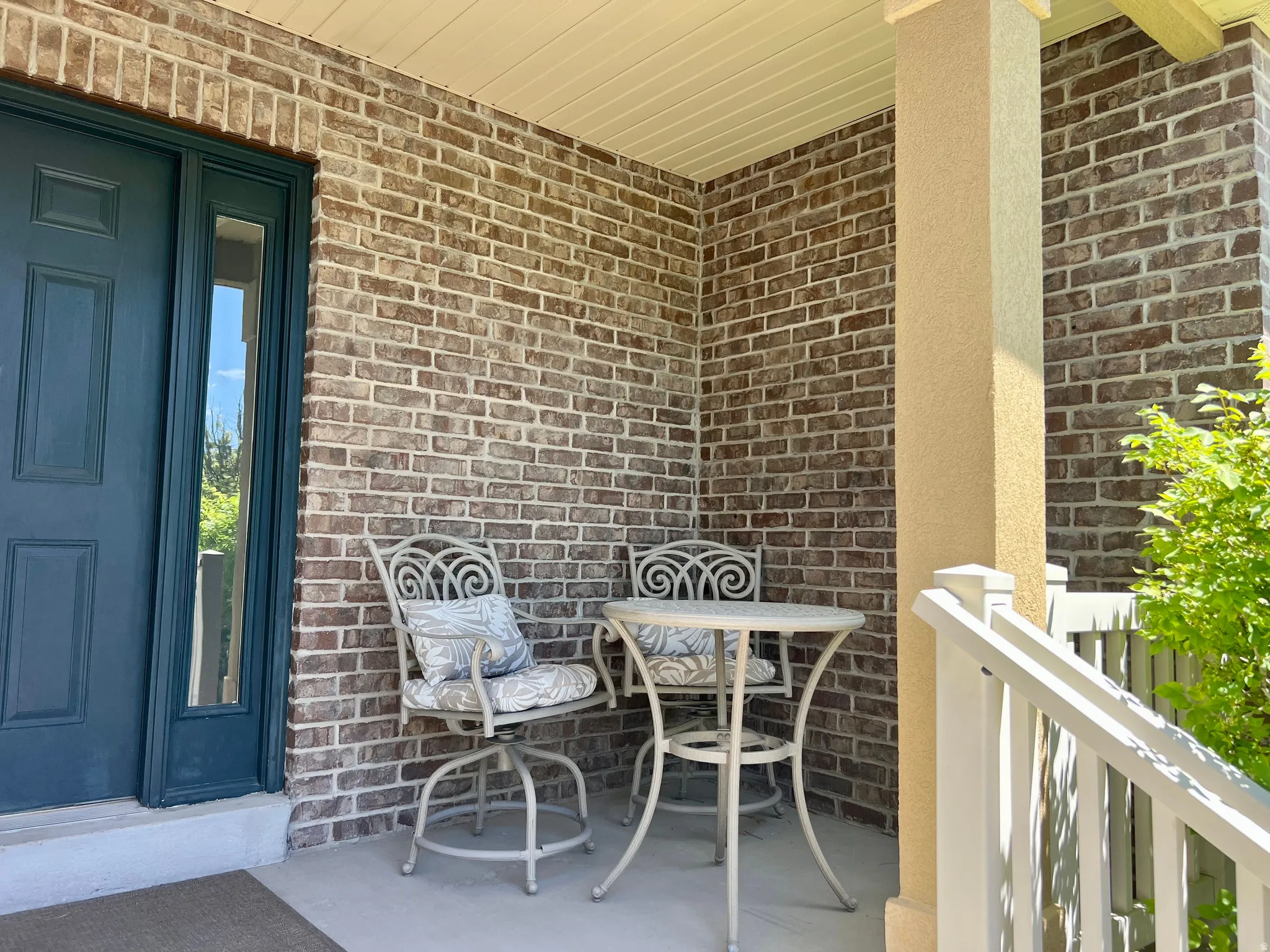 Covered porch featuring a dark teal entry door with sidelight, brick facade, stucco column, and white railings