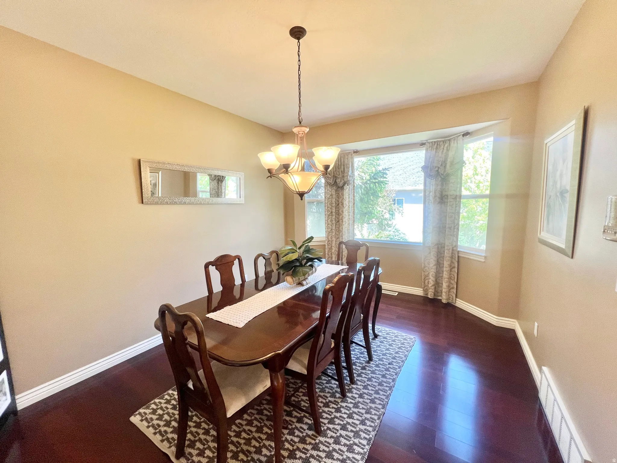 Formal dining space featuring dark wood-finish flooring, a bay window with natural light, and a prominent chandelier