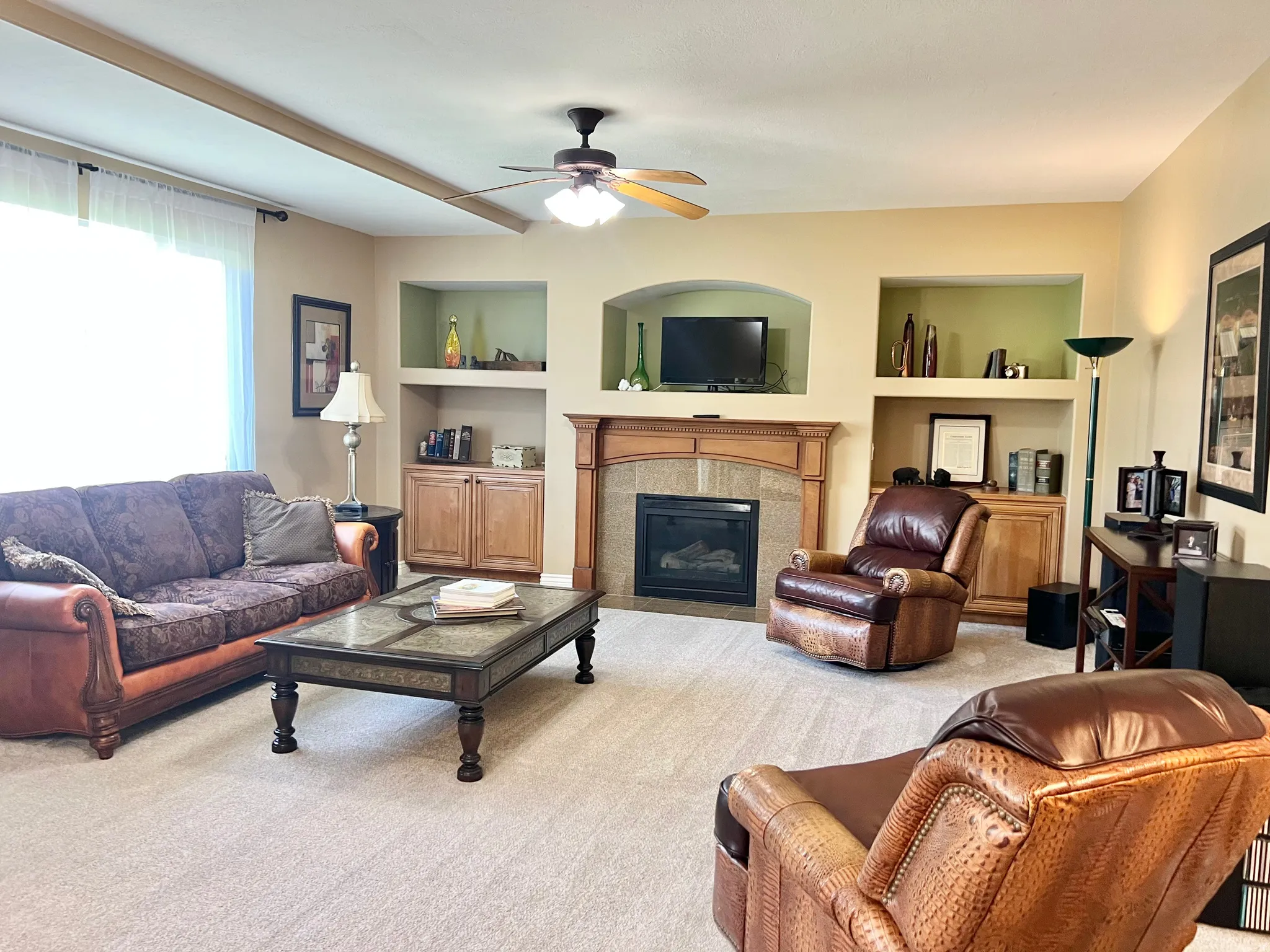 Living area featuring a gas fireplace with a wood mantle, built-in shelving, and a ceiling fan