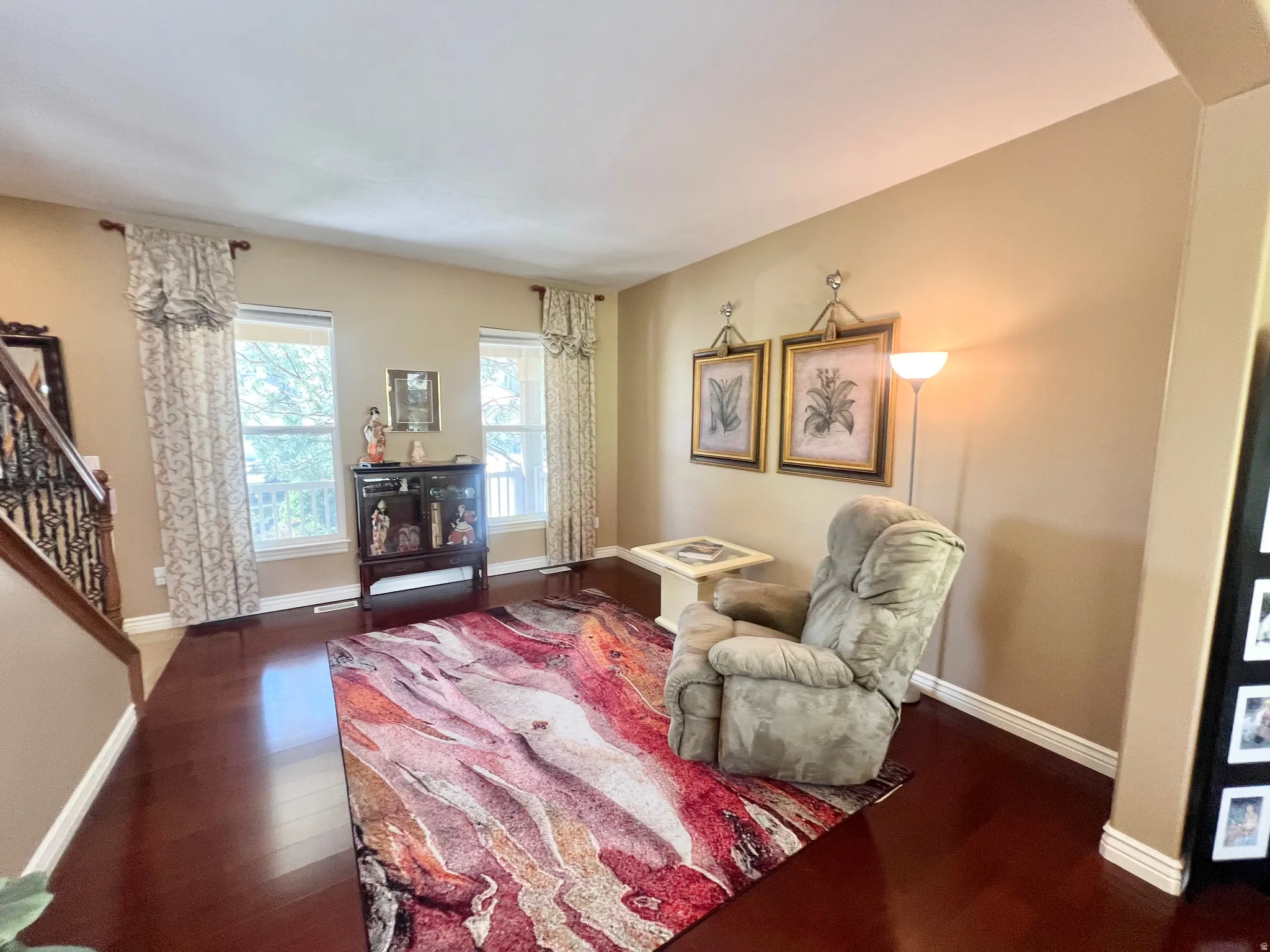Spacious living area featuring rich wood-finish flooring, ample natural light from multiple windows, and neutral wall tones