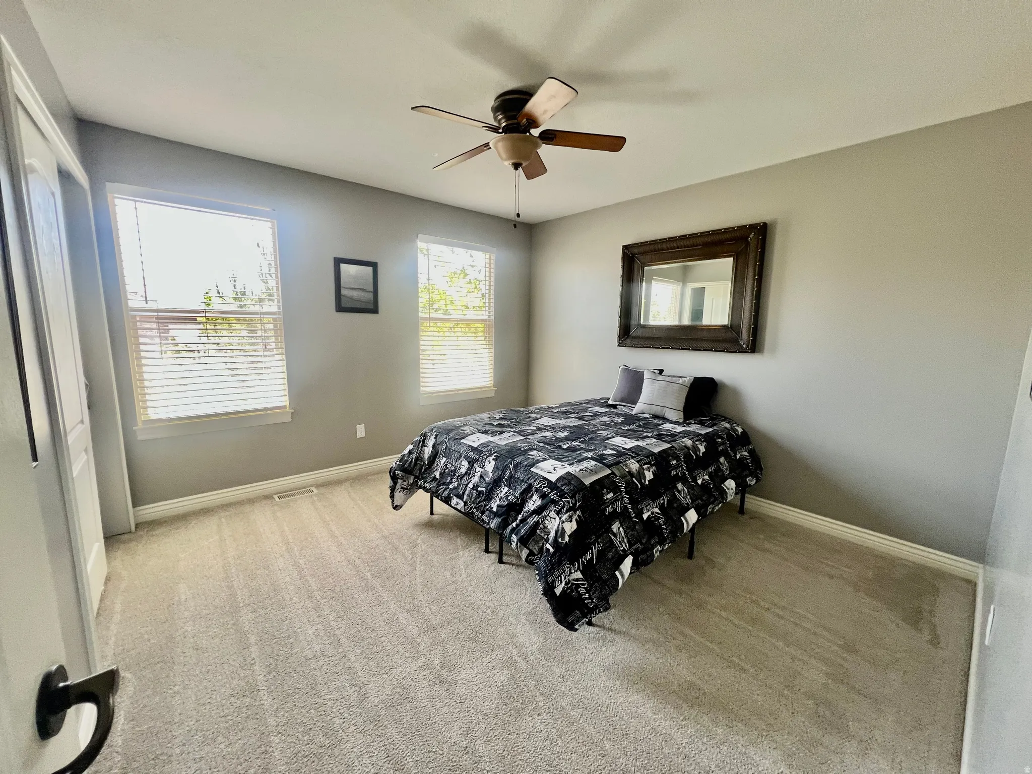 Carpeted room featuring a ceiling fan with light fixture, two windows with blinds, and white baseboards