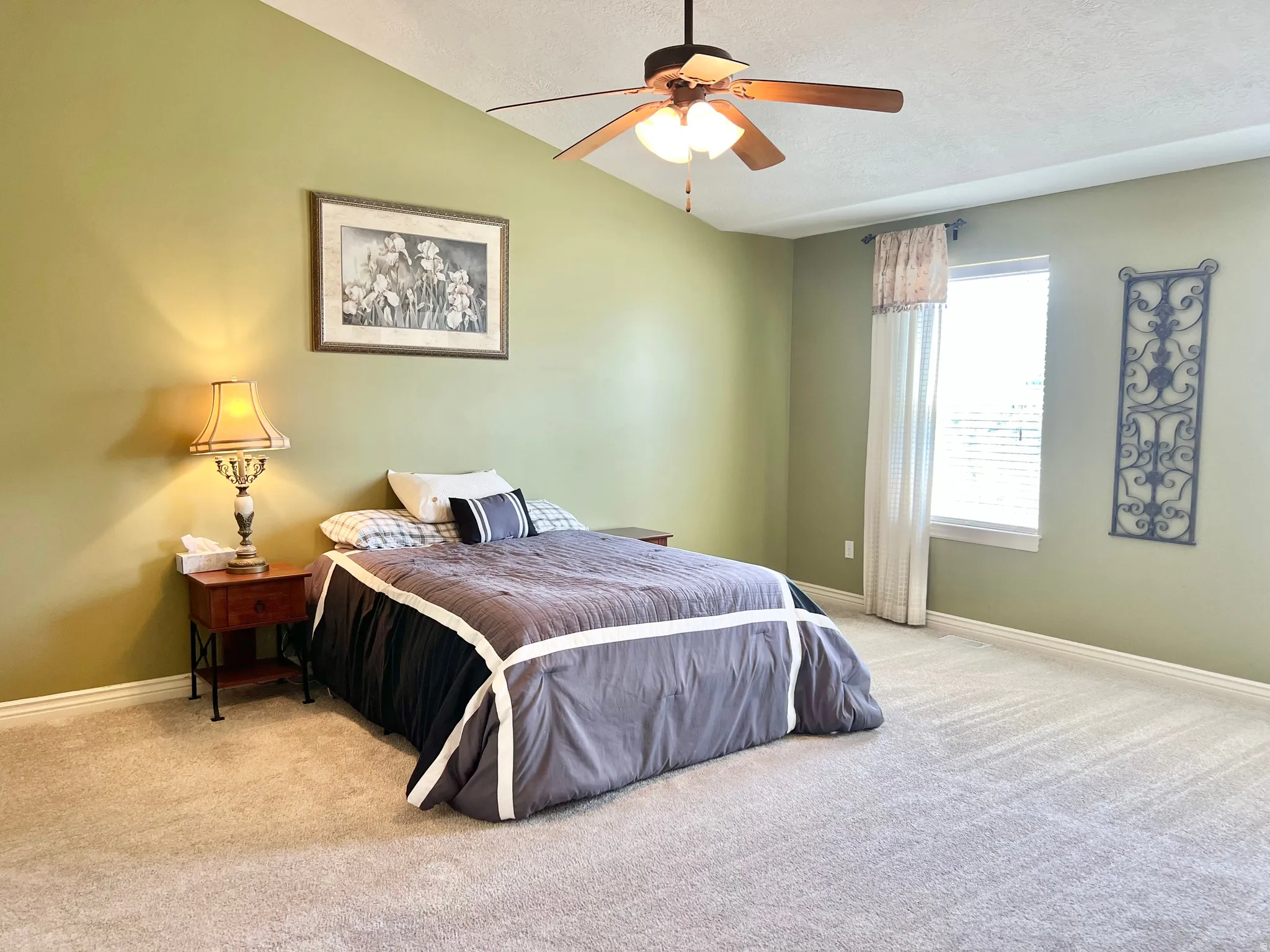 Spacious room featuring vaulted ceilings, a ceiling fan, light-colored carpet flooring, a window with blinds, and light green walls