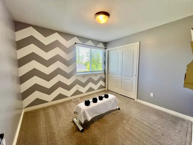 Carpeted room featuring a chevron accent wall, white trim, a double-door closet, and a single window with blinds