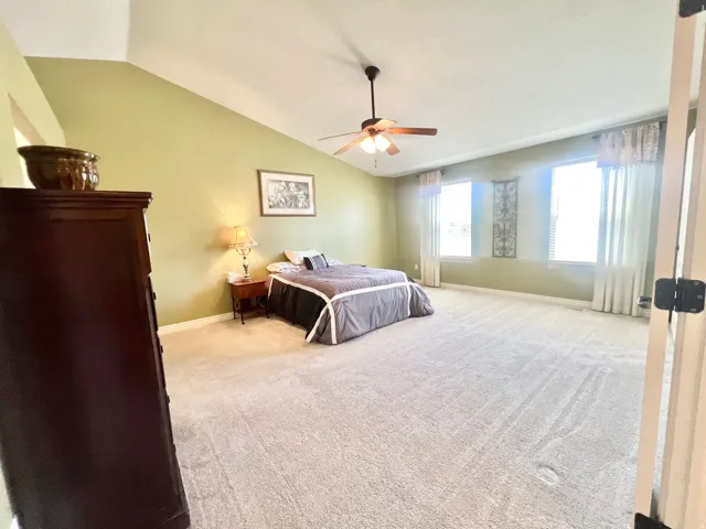 Spacious bedroom featuring vaulted ceilings, light green wall tones, neutral carpet flooring, and a ceiling fan with integrated lighting
