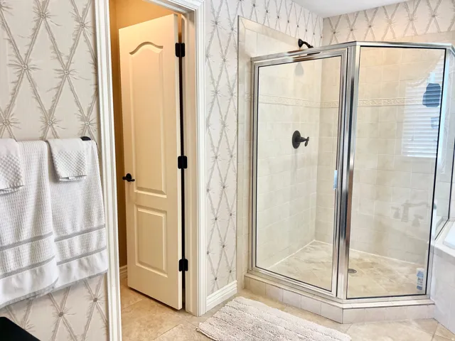 Glass-enclosed shower featuring light-toned tile walls and flooring, complemented by matte black fixtures